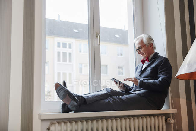 Uomo anziano seduto nel davanzale della finestra con tablet — Foto stock