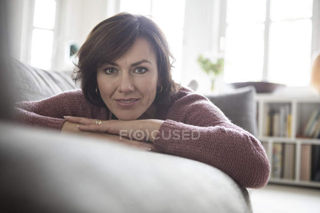 Retrato de mujer tumbada en el sofá en casa y mirando a la cámara - foto de stock