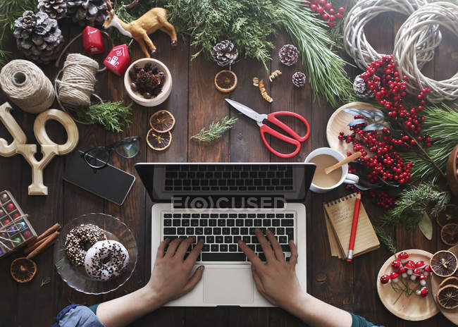 Woman working with laptop at her desk covered with utensils for creating Advent wreaths, partial view — Stock Photo