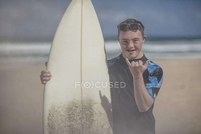 Teenage boy with down syndrome with surfboard on beach — Stock Photo