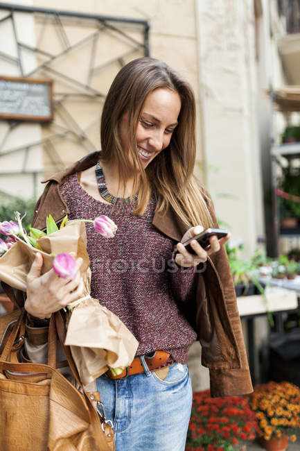 Mulher sorridente com flores e telefone celular ao ar livre — Fotografia de Stock