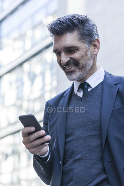 Empresário sorrindo usando telefone celular na frente do prédio de escritórios — Fotografia de Stock