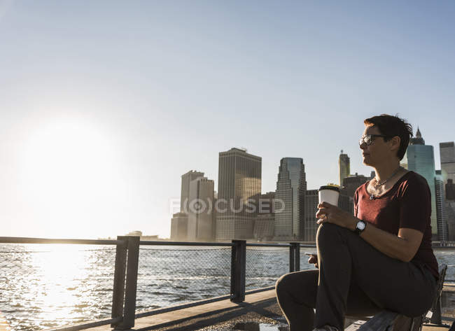 Mulher com café para ir sentado no banco e olhando para a vista — Fotografia de Stock