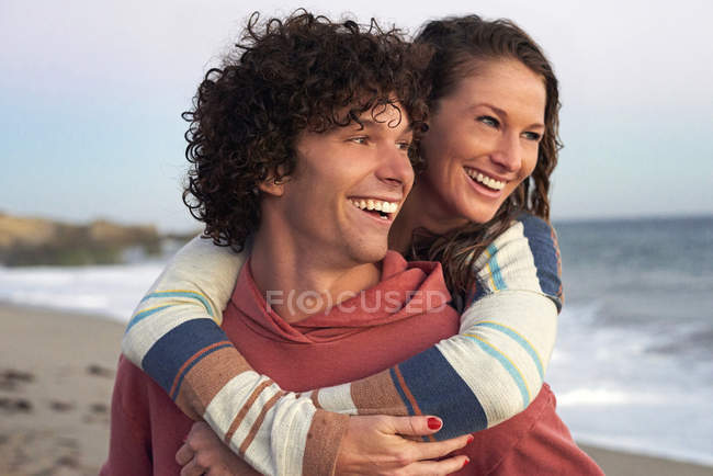 Щасливий молодий чоловік, що носить дівчину з свинарником на пляжі — стокове фото