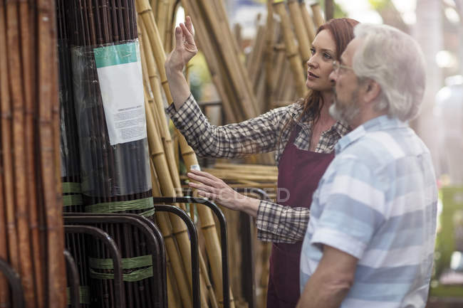 Shop assistent and client in garden centre looking at bamboo fencing — Stock Photo