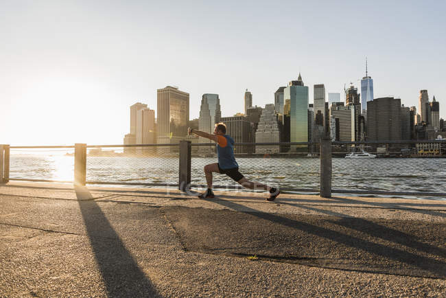 USA, Brooklyn, uomo che fa esercizi di stretching davanti allo skyline di Manhattan la sera — Foto stock