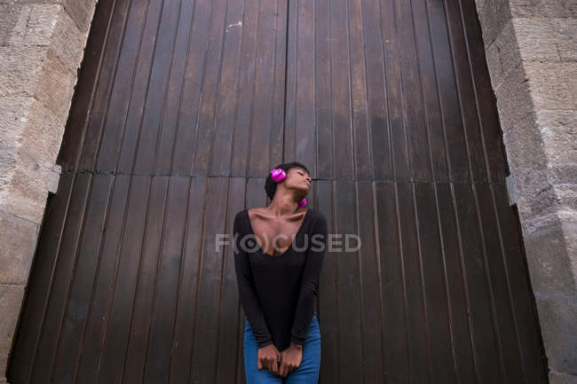 Jeune fille afro-américaine attrayante écouter de la musique dans des écouteurs contre de grandes portes — Photo de stock