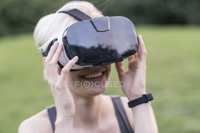Улыбающаяся молодая женщина с помощью очков виртуальной реальности на открытом воздухе — стоковое фото
