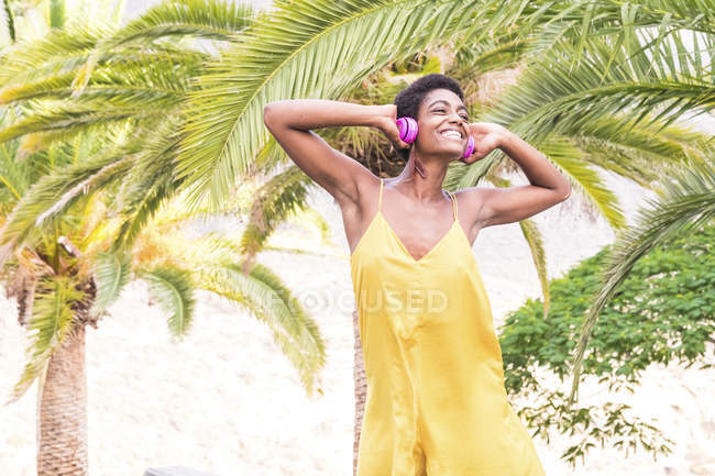 Молодая привлекательная африканская американка в желтом платье слушает музыку в наушниках — стоковое фото