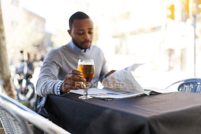 Young man reading newspaper and drinking a beer at street cafe — Stock Photo