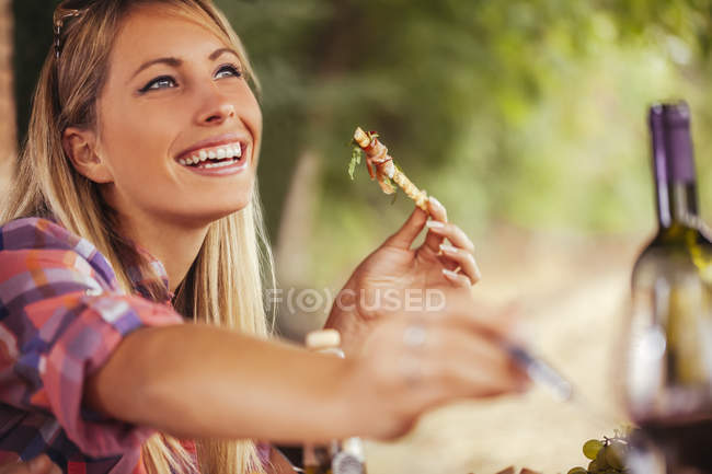Улыбающаяся женщина, которая ест на открытом воздухе днем — стоковое фото