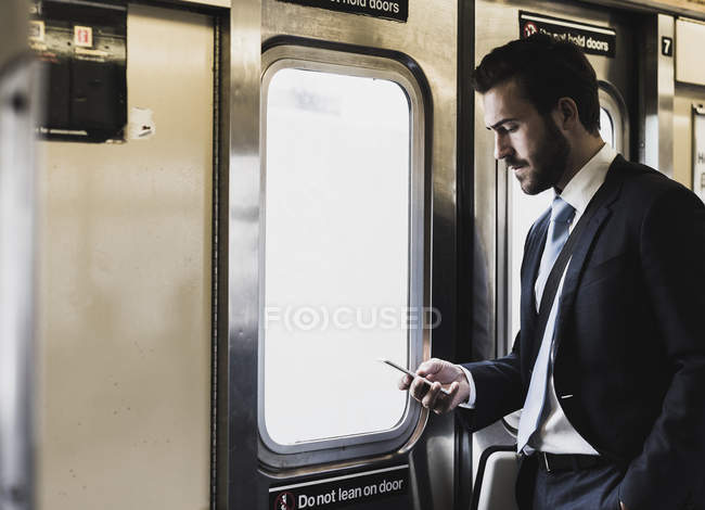 Jovem empresário tomando metrô, usando smartphone — Fotografia de Stock