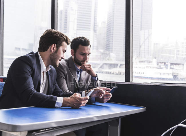 Два бизнесмена с мобильными телефонами разговаривают на пассажирской палубе парома — стоковое фото