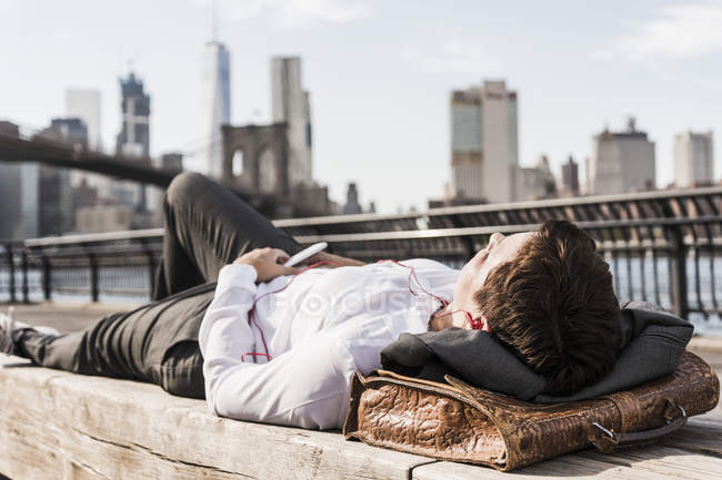 Geschäftsfrau liegend auf Bank Musik hören mit Kopfhörern, brooklyn, usa — Stockfoto