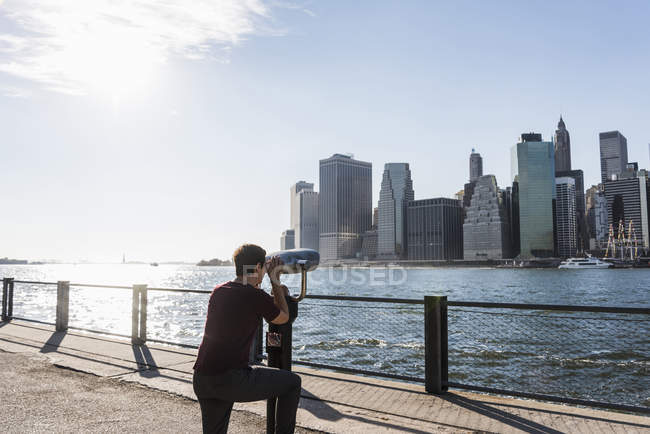 USA, brooklyn, Frau blickt mit Münzfernglas auf die Skyline von Manhattan — Stockfoto
