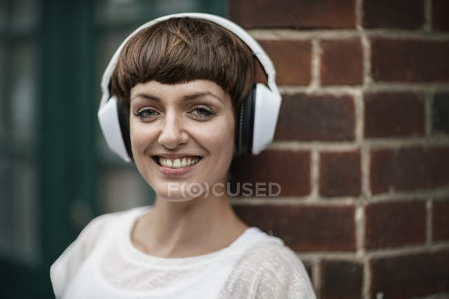 Ritratto di giovane donna sorridente che ascolta musica con cuffie bianche — Foto stock