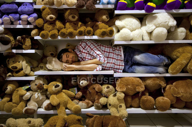 Man sleeping on a shelf between soft toys in a supermarket — Stock Photo