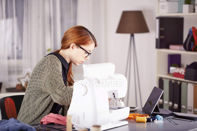 Retrato de mujer joven usando máquina de coser en casa - foto de stock