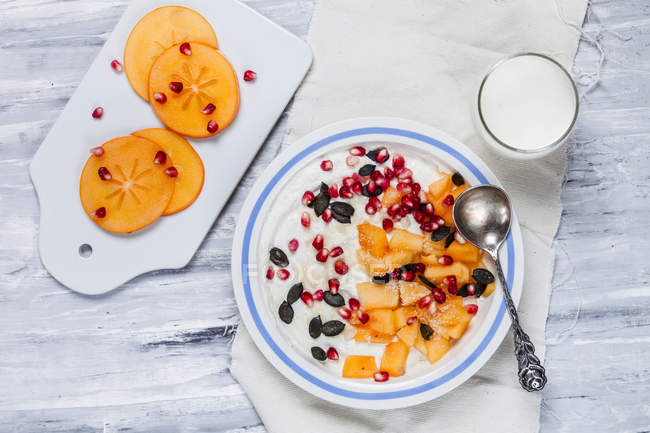 Dish of natural yoghurt, kaki, pomegranate seed, almond and pumpkin seed — Stock Photo