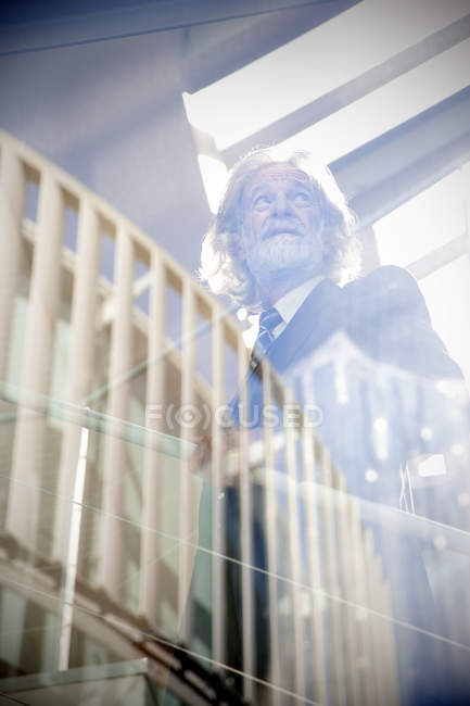 White-haired senior standing on stairs next to window — Stock Photo