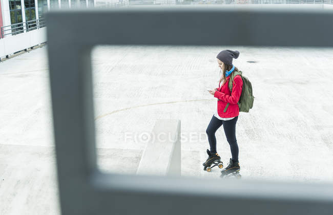 Mujer joven con teléfono celular y patines en línea en el nivel de estacionamiento - foto de stock