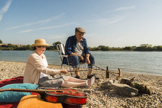 Senior couple barbecueing sausages on the beach — Stock Photo