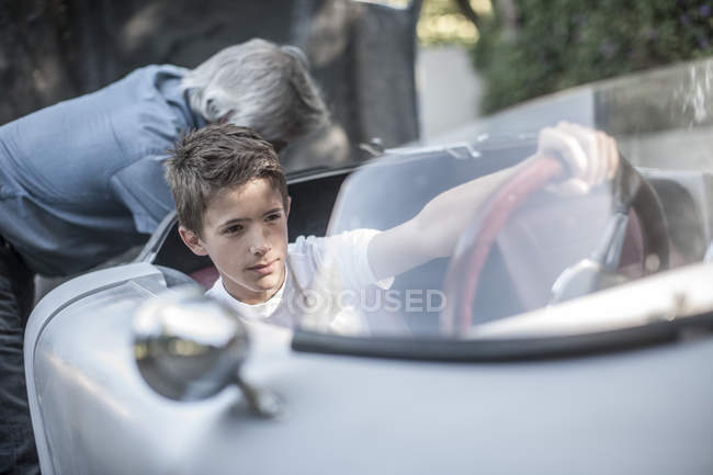 Хлопчик, сидячи в спортивний автомобіль з дідусь на тлі — стокове фото