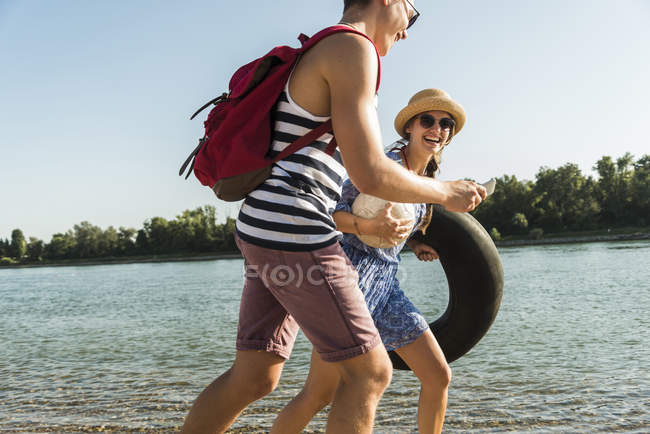 Молодая пара с внутренней трубкой и сотовым телефоном на берегу реки — стоковое фото