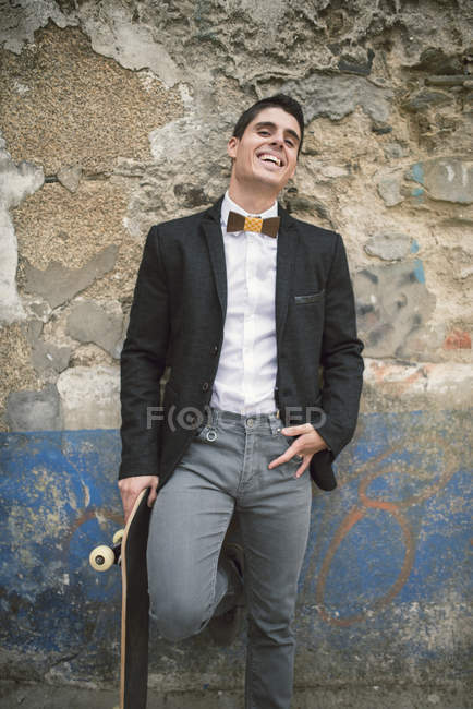 Portrait of young man with skateboard wearing jacket and a wooden bow tie — Stock Photo