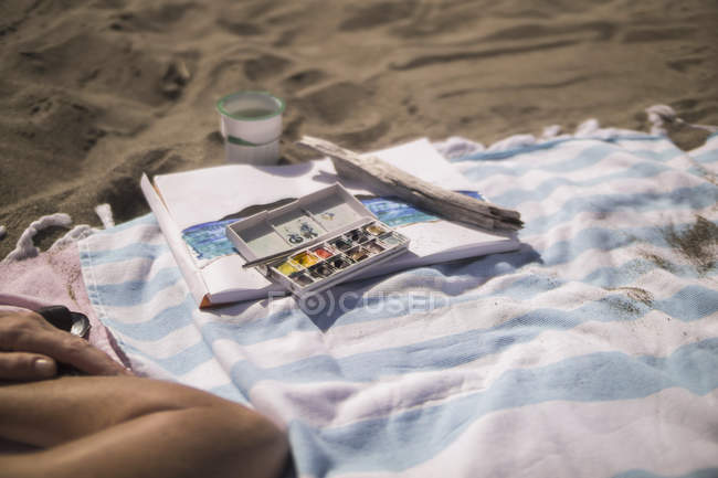 Woman lying next to paintbox on beach towel — Stock Photo