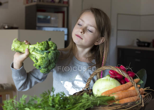 Retrato de niña con canasta de mimbre de verduras frescas mirando brócoli - foto de stock