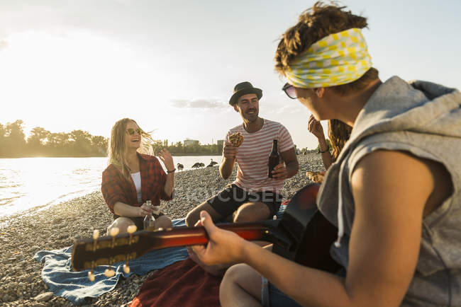 Freunde mit Gitarre entspannen am Flussufer bei Sonnenuntergang — Stockfoto