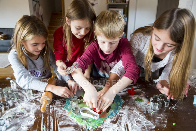 Four children cutting out Christmas cookies at home — Stock Photo
