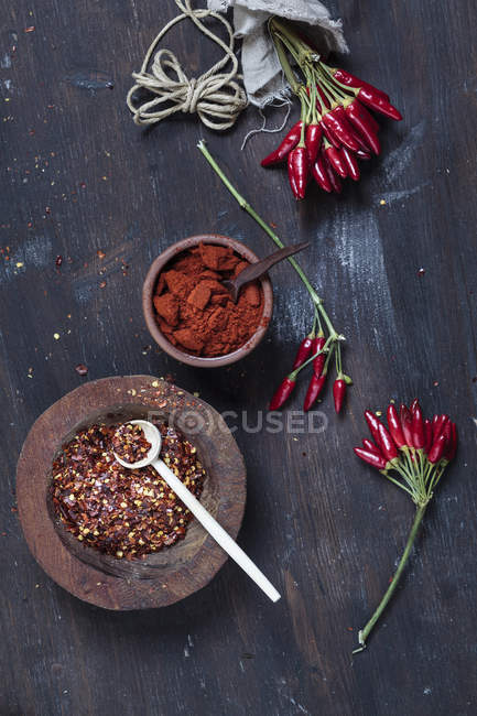 Пучки червоний перець чилі, плити chili пластівці та чаші з порошку чилі по дереву — стокове фото
