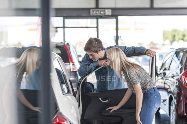 Jeune couple examinant une nouvelle voiture chez un concessionnaire automobile — Photo de stock