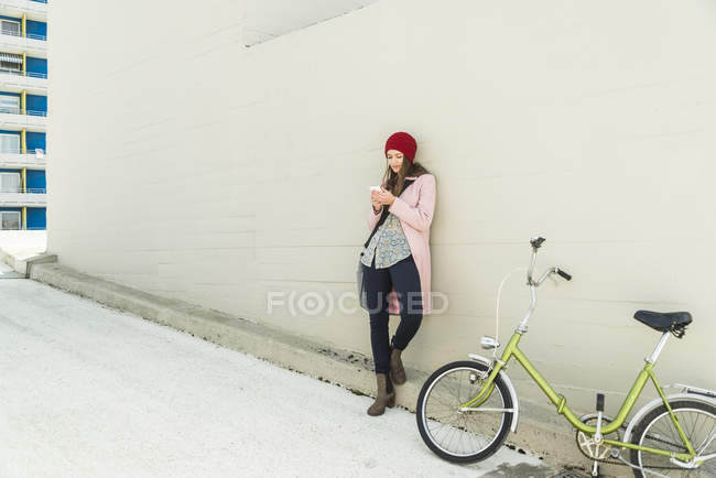 Giovane donna accanto alla bicicletta guardando il cellulare — Foto stock