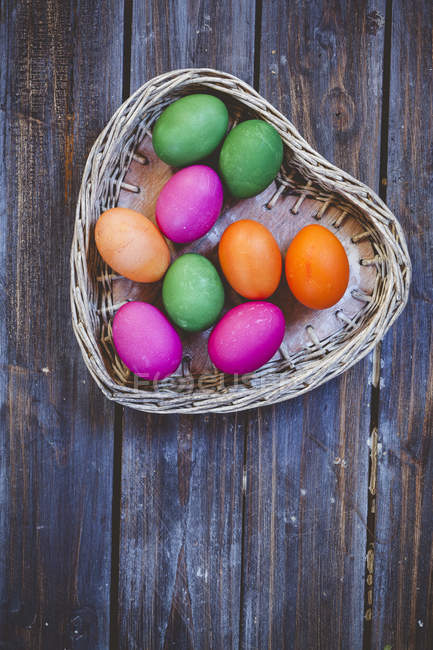 Зеленые, розовые и оранжевые пасхальные яйца в плетеной корзине — стоковое фото