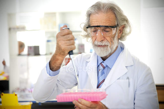 Professor sênior enchendo copos de amostra em laboratório — Fotografia de Stock