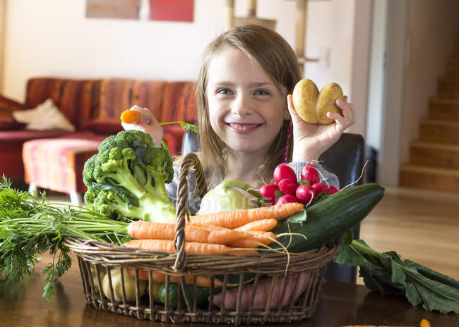 Porträt eines grinsenden Mädchens mit Weidenkorb mit frischem Gemüse zu Hause — Stockfoto