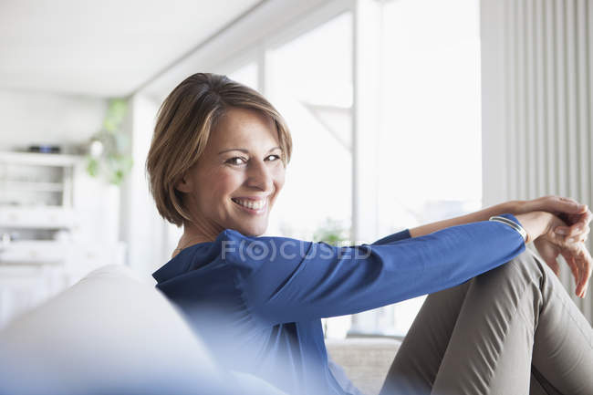 Femme souriante à la maison assise sur le canapé — Photo de stock