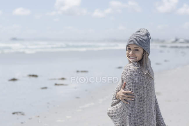 Retrato de mulher sorridente vestindo gorro e envoltório na praia — Fotografia de Stock