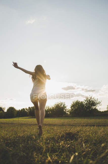 Vista posteriore della donna che corre a piedi nudi su un prato alla retroilluminazione — Foto stock