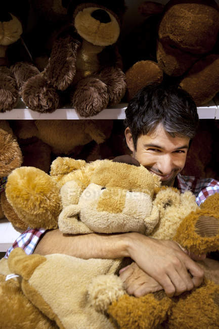 Uomo sorridente che abbraccia orsacchiotti in un negozio — Foto stock