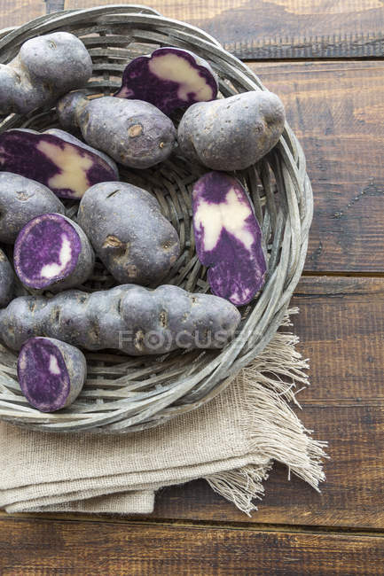 Sliced and whole purple potatoes in a wickerbasket — Stock Photo