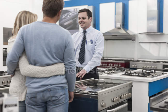 Помощник продавца разговаривает с молодой парой торговых кухонного оборудования — стоковое фото