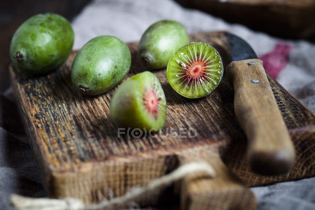 Sliced and whole mini kiwis and kitchen knife on wooden chopping board — Stock Photo