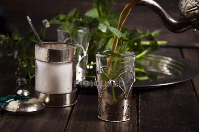 Verter té negro en un vaso de té con hojas de menta fresca - foto de stock