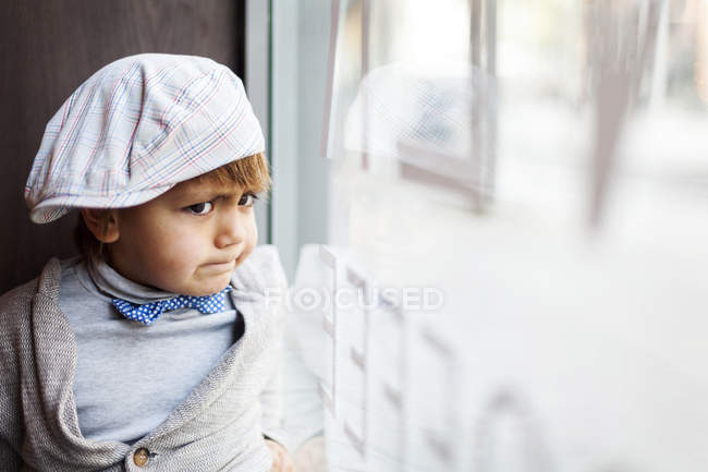 Ritratto di ragazzino arrabbiato con cappuccio che guarda attraverso la finestra — Foto stock