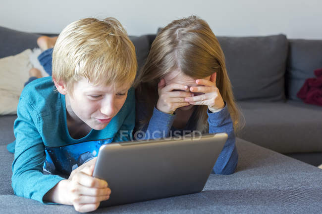 Хлопчик і дівчинка, лежачи на дивані, використовуючи цифровий планшетний — стокове фото