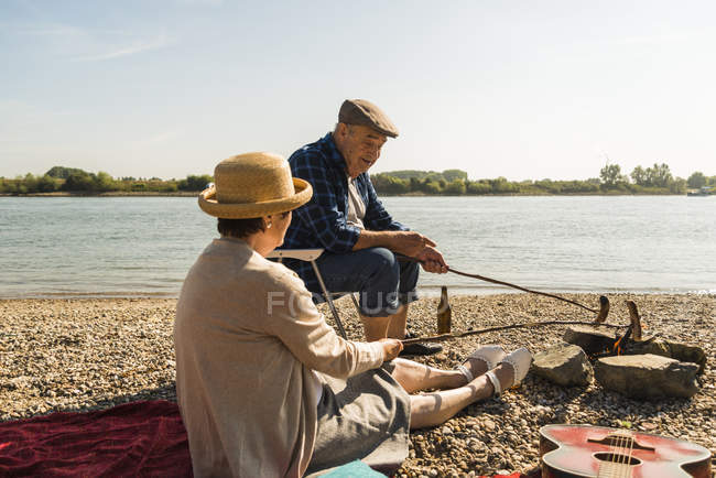 Anziani coppia barbecue salsicce sulla spiaggia — Foto stock